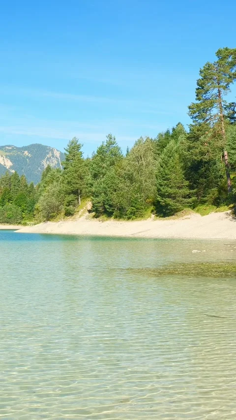 Turquoise lake Urisee surrounded by pine forests and rugged hills in Reutte T Stock Footage 308302175