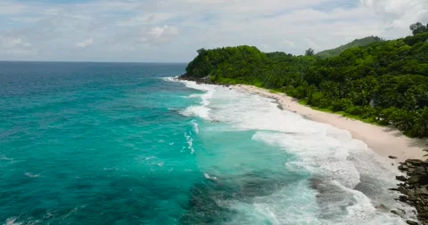 Turquoise ocean waves and white sandy beach with green hills. Seychelles, Mahe. 스톡 동영상 345381218