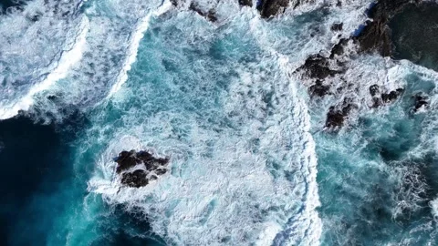 Turquoise ocean waves crash against rocky shoreline, creating foam and splashes Stock Footage 328296977