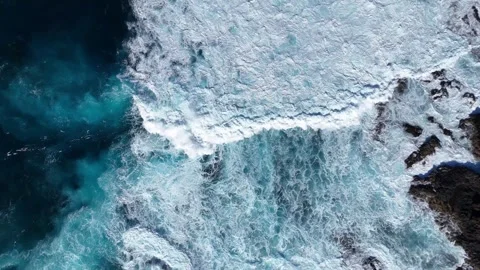 Turquoise ocean waves crash against rocky shoreline, creating foam and splashes Video stock 330167543