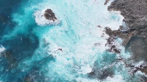 Turquoise ocean waves crash against rocky shoreline, creating foam and splashes Stock Footage 331821092