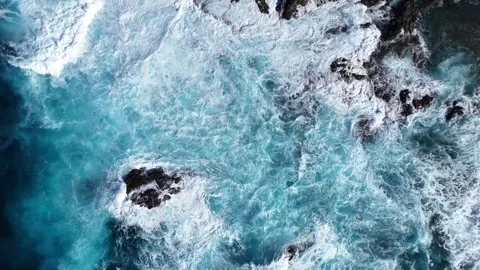 Turquoise ocean waves crash against rocky shoreline, creating foam and splashes Vidéo 335877889