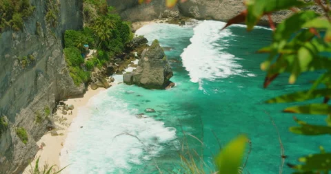 Turquoise ocean waves crash against white sand beach below steep cliffs of Nusa Stock Footage 344916756