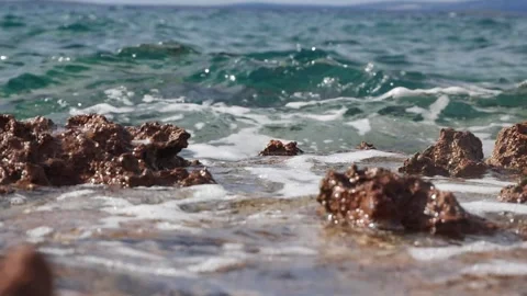 Turquoise ocean waves crash gently against brown jagged coastal rocks. Stock Footage 337407353
