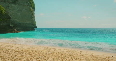 Turquoise ocean waves crash onto white sand beach below green cliff at Video stock 343371213