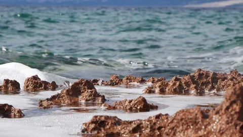 Turquoise ocean waves gently washing over brown rocky coastal shore. Stock Footage 337405506