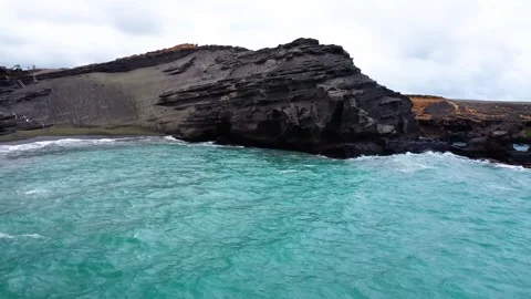 Turquoise ocean waves meeting dramatic volcanic cliffs and black sand beach Stock Footage 312610547