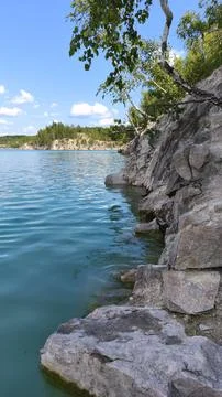 Turquoise quarry lake bordered by rugged rocky cliffs and green forest 写真素材