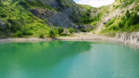 Turquoise quarry lake reflects cliffs below green slopes Video stock 323885569