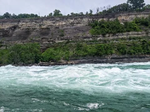 Turquoise rapids flow on the Niagara River with layered limestone Stock Photos