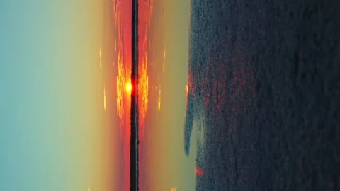 Turquoise red and pink sunset sun and clouds reflected in the water vertical Stock Footage 256993733