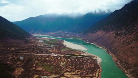 Turquoise river bend beside fields and village below low clouds in Tibet Video stock 345884125