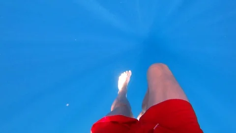 Turquoise sea with sun rays. Partial view of swimming men in red shorts Stock Footage 113010932