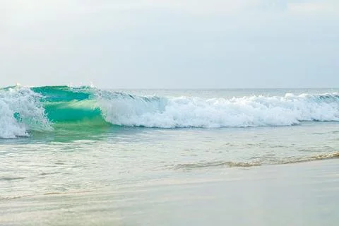Turquoise sea wave rolls onto the flat, gently sloping shore of the sandy bea Stockfoto's