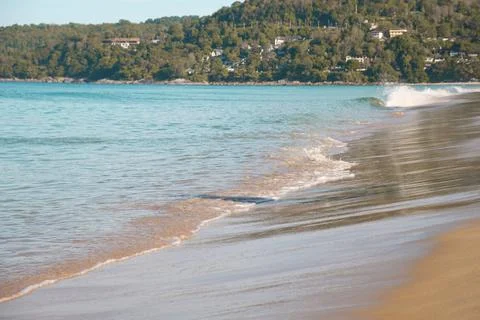 Turquoise sea wave rolls onto the flat, gently sloping shore of the sandy bea Stock Photos