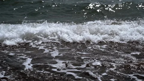 Turquoise sea waves break on the rocky coastline, forming foam. A Video of dark Stock Footage 192998414