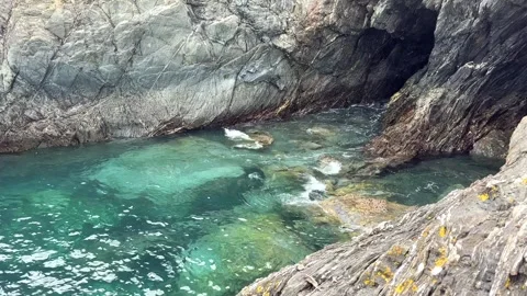 Turquoise Waters Flow Through Rocky Inlet and Sea Cave in Falmouth, Cornwall Видео 336785395