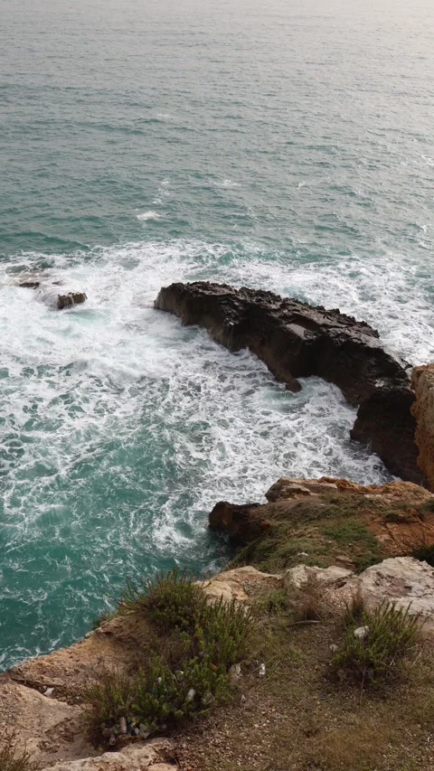 Turquoise waves crash against rugged coastal rocks Stock Footage 328287083