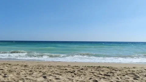 Turquoise Waves Crashing on a Sandy Beach Under a Clear Blue Sky Stock-Footage 296795178