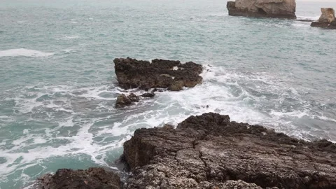 Turquoise waves swirling around rugged coastal rocks Stock Footage 328286938