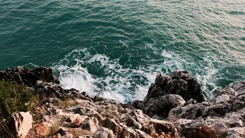 Turquoise waves wash over rugged cliffside rocks along Mediterranean shoreline Stock Footage 328932705