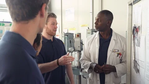 Tutor Discussing Technical Drawings With Apprentice Engineers Stock Footage 86602028