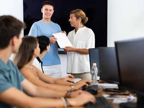 Tutor presenting certificate of completion of computer courses to satisfied guy 写真素材