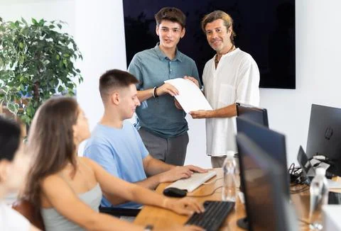 Tutor presenting certificate of completion of computer courses to satisfied guy 写真素材