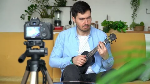 Tutorial, online music training. Male blogger records video playing guitar. 動画素材 157830476