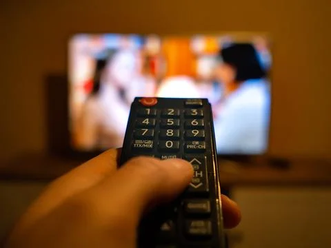 TV controller pointing to the switched on TV Stock Photos