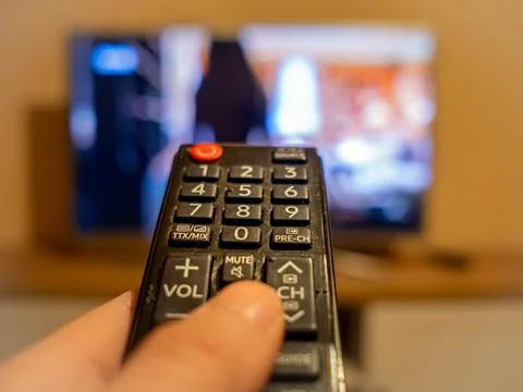 TV controller pointing to the switched on TV Stock Photos