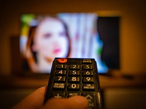 TV controller pointing to the switched on TV Stock Photos