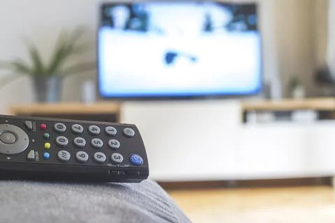 TV remote control in the foreground, tv in the blurry background. Streaming Stock Photos