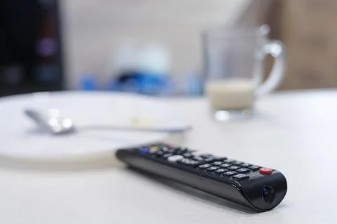 TV remote control on table, in kitchen next empty plate and cup, end breakfast Foto stock