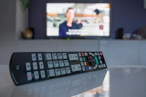 TV remote controller on coffee table in front of smart television set Stock Photos
