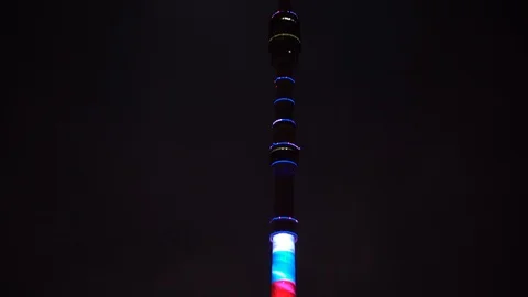The TV tower is lit by a multi-colored illumination, near the full moon. Night Stock Footage 106355670