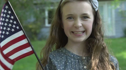 A tween girl smiles at camera in front of her house holding a US flag Stock Footage 44117524