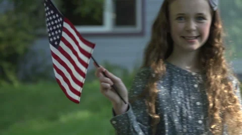 A tween girl smiles at camera in front of her house waving a US flag Stock Footage 44117527