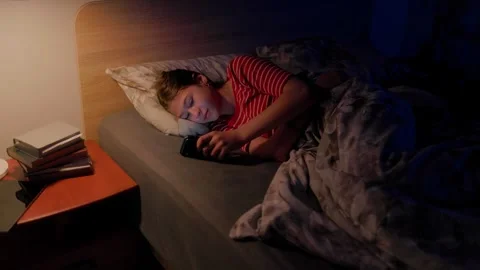 Tween using mobile phone in bed under warm lamp light late at night in bedroom Stock Footage 336669738
