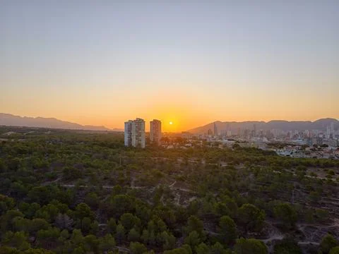 Twilight casts warm glow overlooking city, evening sunset behind forest and.. Stock Photos