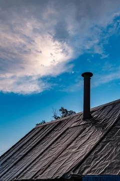 Twilight glow over rustic rooftop with roofing felt and metal chimney Stock Photos