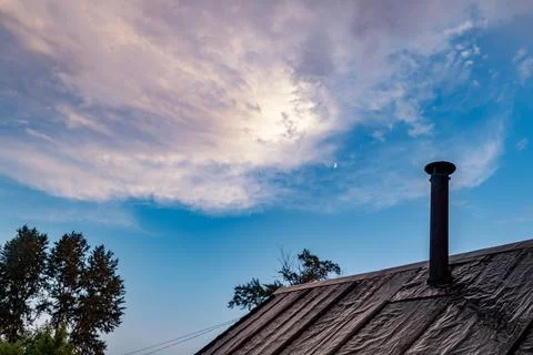 Twilight glow over rustic rooftop with roofing felt and metal chimney Stock Photos