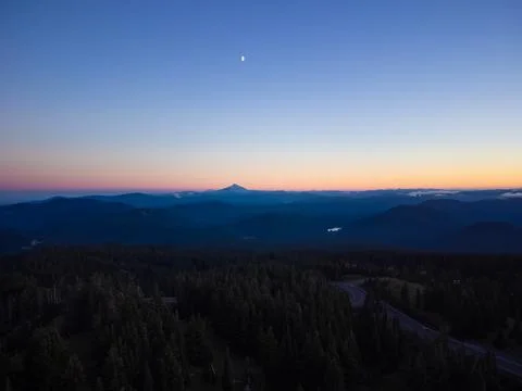 Twilight. Pine forest, mountain range and highway. The sky is colored orange  Stock Photos