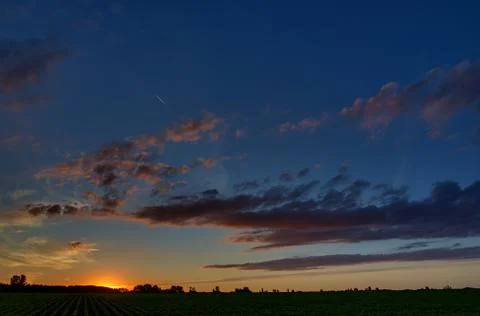 Twilight sky with clouds at dawn over a field with agricultural plantations. Stock Photos