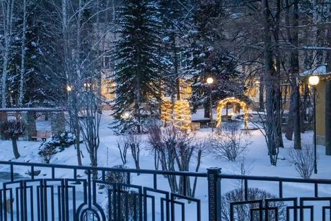 Twilight winter park with string lights and wrought-iron fence, cozy cityscap Stock Photos