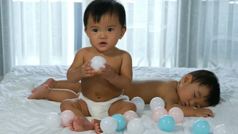 Twin babies on a bed, one playing color ball, one sleeping Video stock 135508119