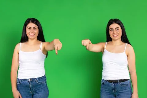 Twins in identical clothes point down with their index finger. Green background Stock-Fotos