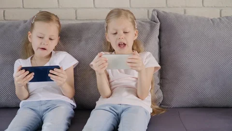 Twins using smatphones on sofa 스톡 동영상 107399850