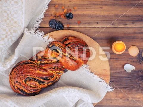 Twisted loaf with poppy seeds and chicken egg with yolk and broken shells on a Stock Photos