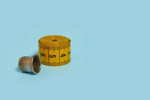 A twisted tailor's meter and a thimble on a blue background, close up Stock Photos